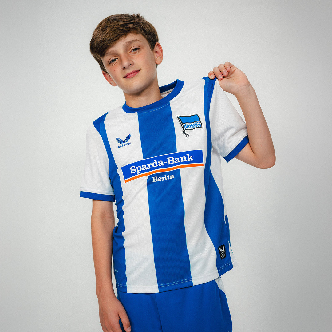 Hertha Heimtrikot Kids 26/27 Modelbild mit Trikot in der Hand